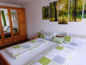 Une chambre à coucher avec un grand lit, une armoire en bois et trois tableaux représentant des paysages forestiers, accrochés au mur.