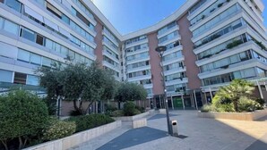 Un edificio residencial de varios pisos con balcones, un patio central y abundante vegetación alrededor.