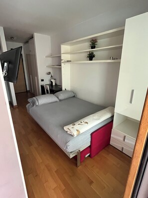 A bedroom with a bed, a desk, a chair, a TV, and a wardrobe.