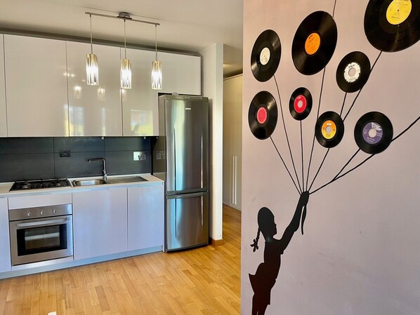 A modern kitchen with stainless steel appliances, pendant lighting, and a wall art installation of vinyl records.