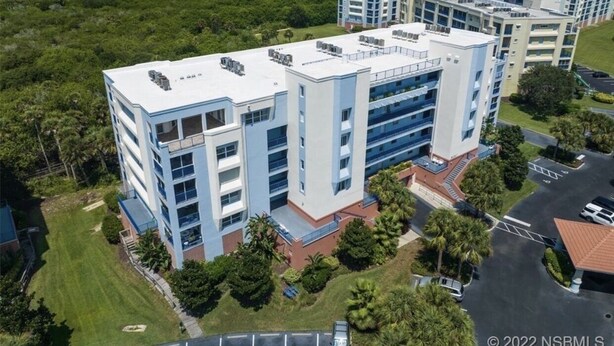 A modern multi-story hotel with a flat roof, multiple balconies, and a parking area.