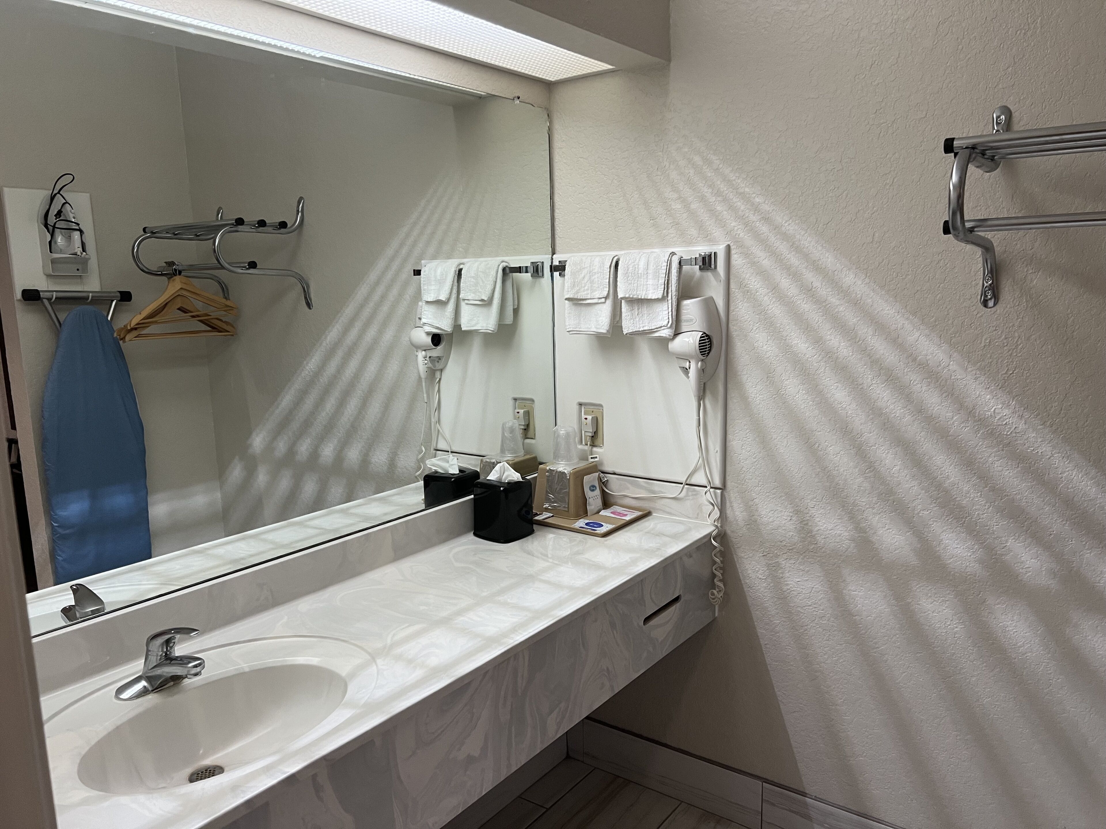 Un baño moderno con un espejo grande, lavamanos blanco y perchero para toallas.