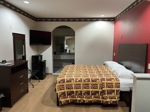 A hotel room with a bed, a desk, a dresser, a TV, and a bathroom visible through an archway. - Scott Inn Suites - Downtown Houston (Houston)