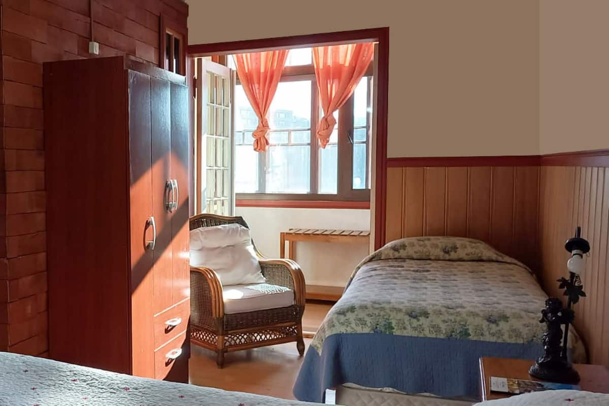 A room with a bed, a chair, a wardrobe, and a window with curtains.
