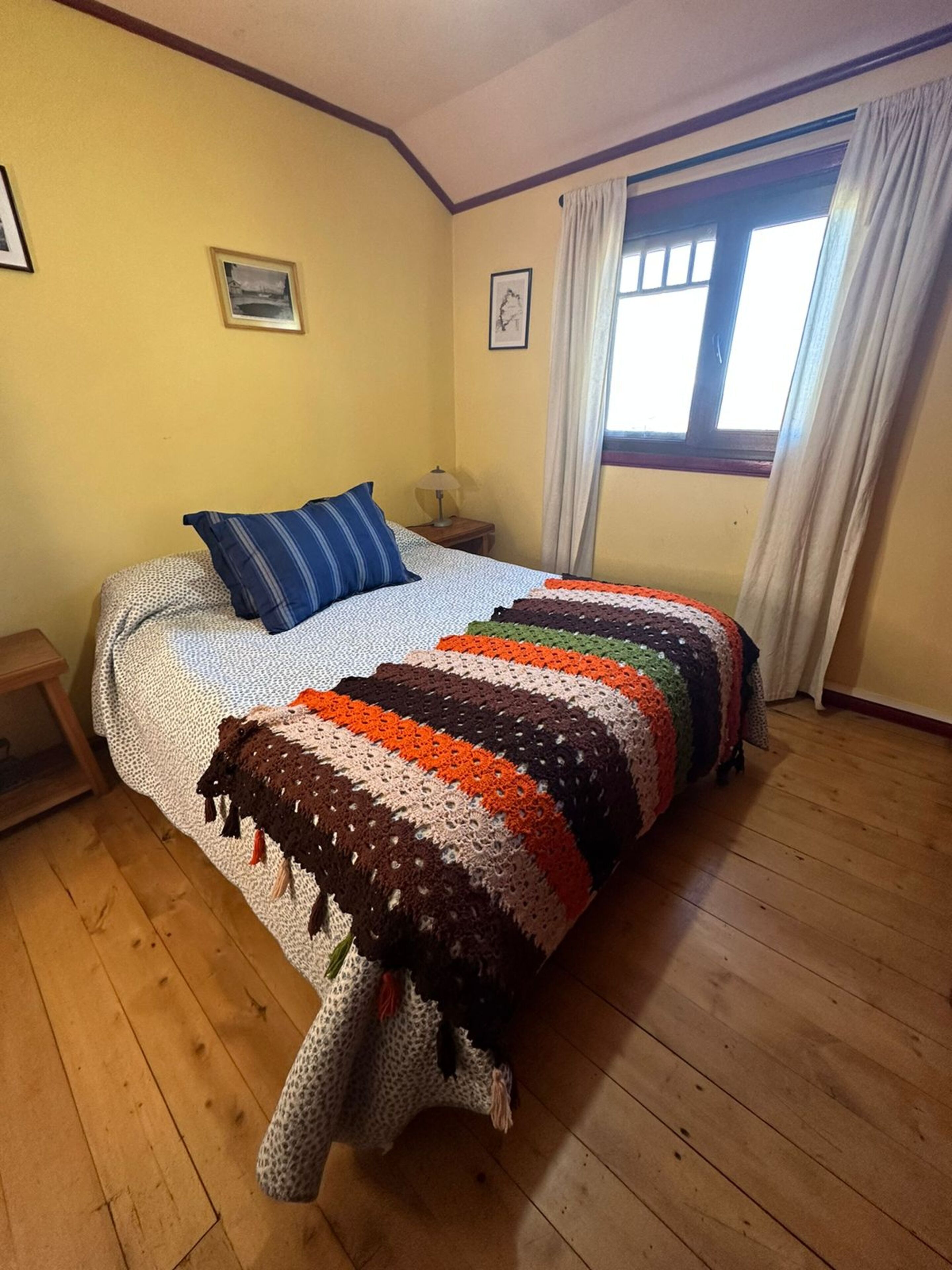 A bedroom with a bed, a nightstand, a window with curtains, and a wall with a picture.