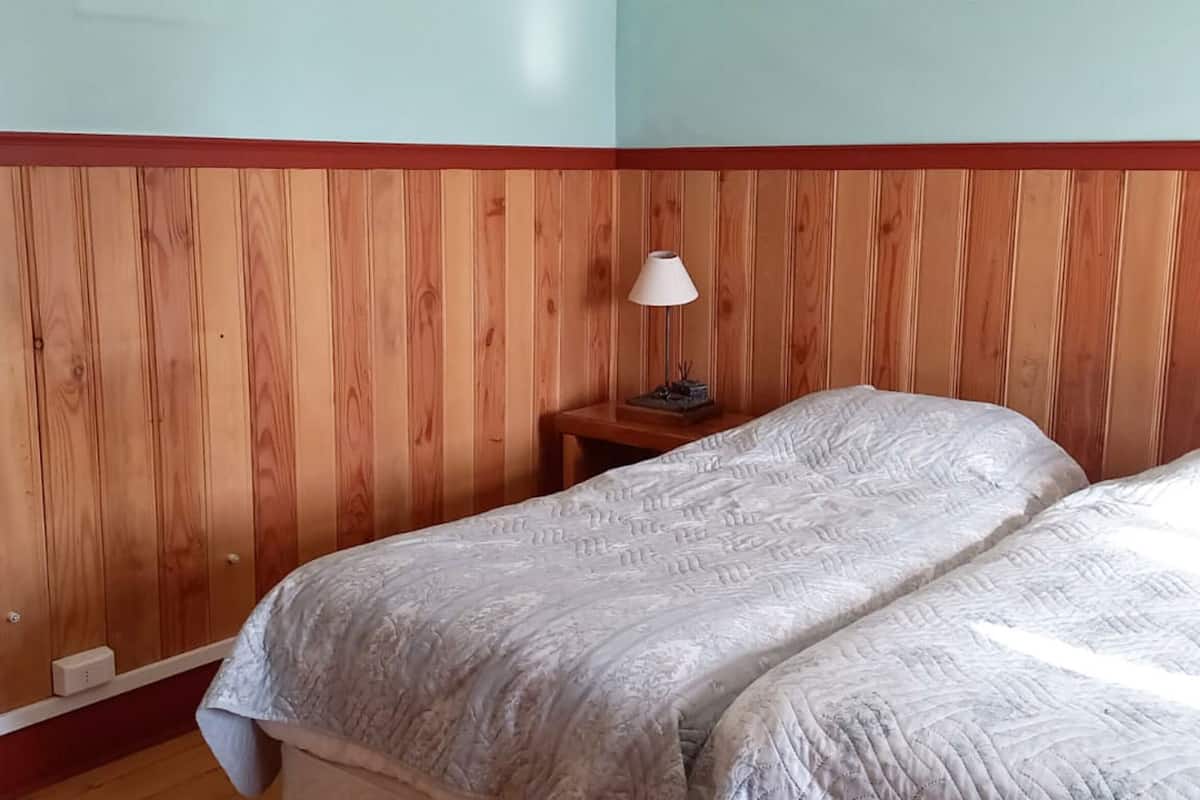 A room with wooden panel walls, a bed with a patterned bedspread, and a bedside table with a lamp.