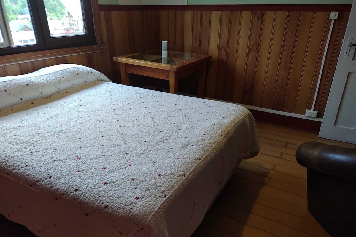 A room with a bed, a small wooden table, and a window.