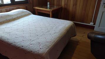 Una habitación con una cama, una mesita de madera y un ventanal.