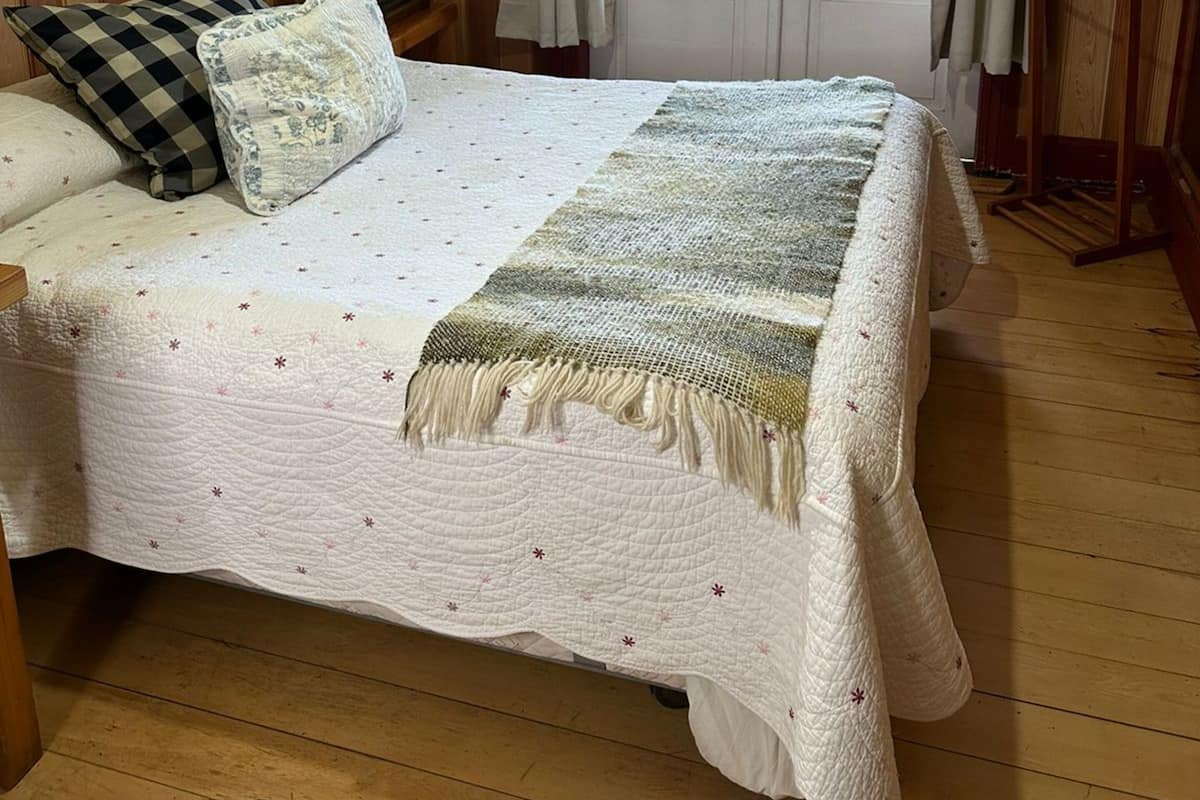 A room with a bed, wooden floor, a window with curtains, and a door.