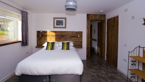 A bedroom with a large bed, a wooden headboard, a window with curtains, a picture on the wall, and a ceiling light.
