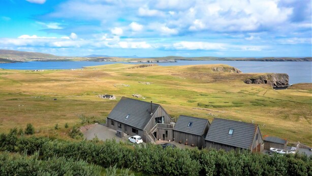A rural landscape with a large barn and a small house, surrounded by fields and a body of water.