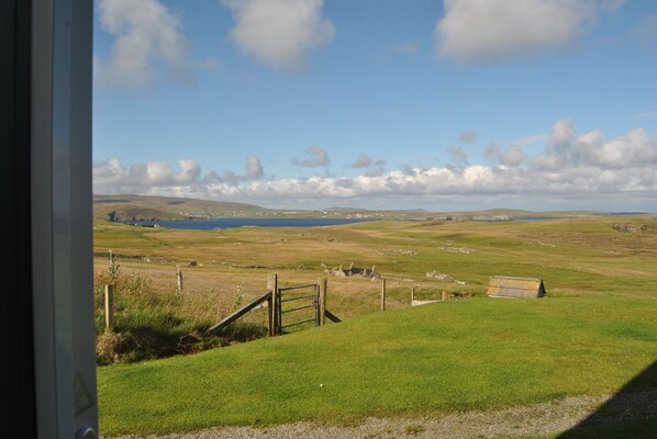 A rural landscape with a grassy field, a small gate, and distant hills. - Voortrekker apartments - Soothpunds - Hot Tub & Sauna area (Levenwick)