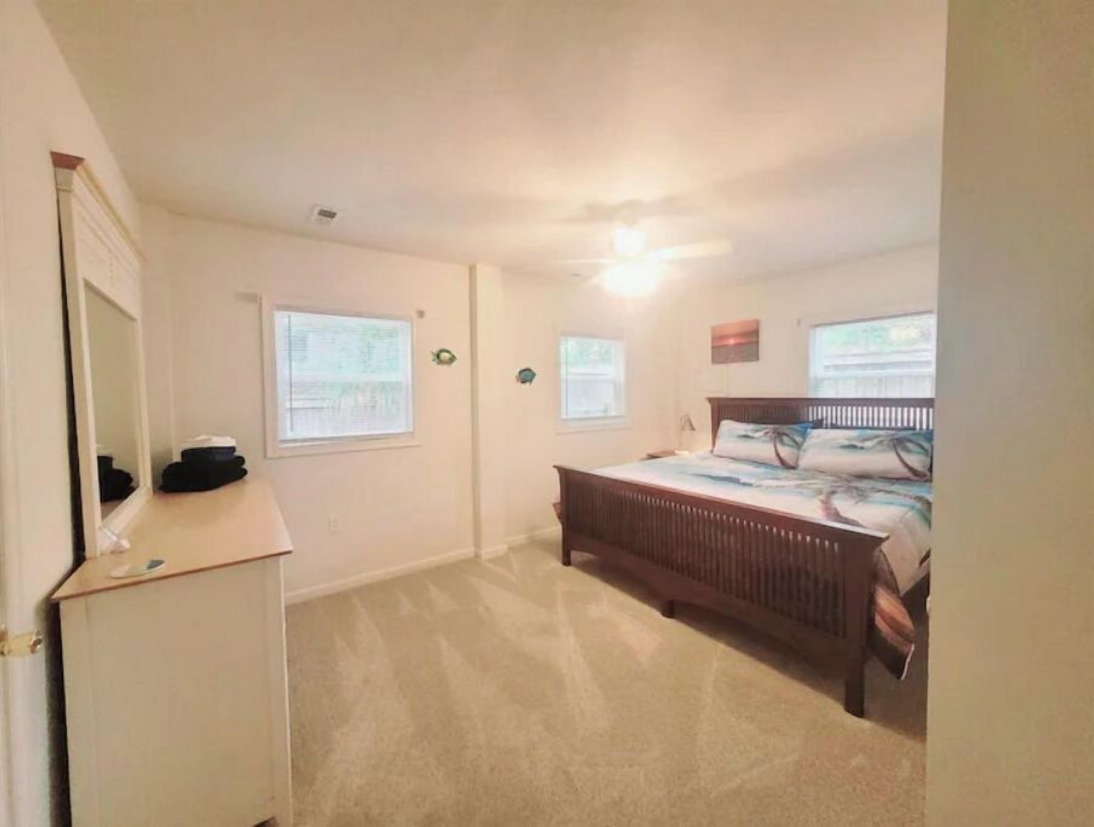 A bedroom with a bed, a dresser, and a mirror. There are two windows and a ceiling light.