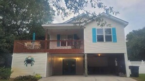 A two-story house with a front porch, a garage, and a small garden area. - OBX~Beach~Sunsets~Bike Path~Mini Golf~Lighthouses~Shops~Walking Distance~Sunrise (Kill Devil Hills)