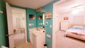 A bedroom with a bed, a dresser, and a bathroom with a sink and mirror. - OBX~Beach~Sunsets~Bike Path~Mini Golf~Lighthouses~Shops~Walking Distance~Sunrise (Kill Devil Hills)