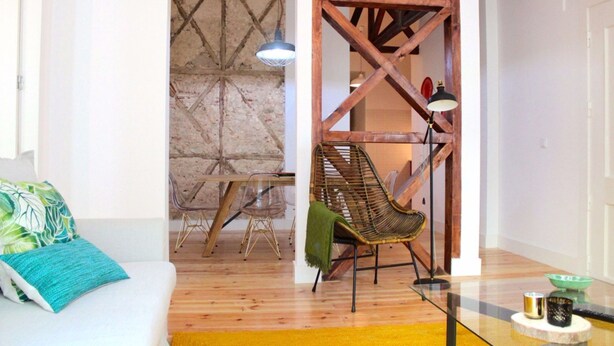 Um quarto com piso de madeira, um sofá branco com almofada verde, uma cadeira suspensa e uma escada de madeira.
