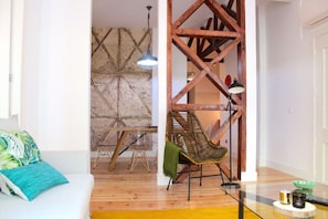A room with a wooden floor, a white sofa with a green pillow, a hanging chair, and a wooden staircase.