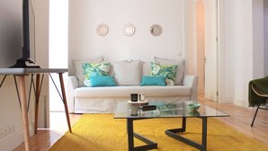 Uma sala de estar moderna com um sofá branco, uma mesa de centro de vidro e uma televisão sobre um móvel.