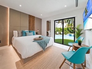 Quarto moderno com uma cama grande, vista para uma piscina e área de jantar com cadeiras.