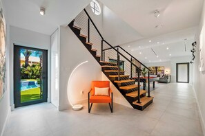 Un intérieur moderne avec un escalier, un fauteuil et une vue sur une piscine.
