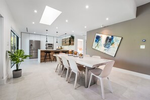 A modern kitchen with a dining area, featuring a large table and chairs, a refrigerator, and a pendant light.