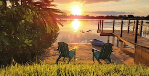 Une vue au coucher du soleil sur un lac paisible, avec un quai, des chaises et un bateau.