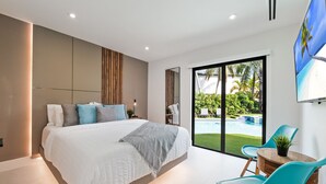 Una camera da letto moderna con un letto grande, vista su una piscina e un'area pranzo con sedie.