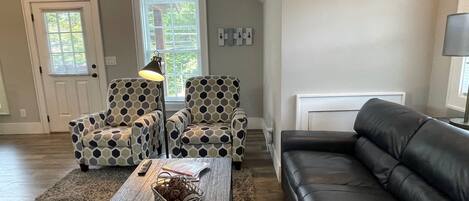 A living room with a black leather sofa, patterned armchairs, a wooden coffee table, and a floor lamp.