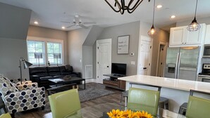 A modern living room with a glass dining table, green chairs, a black leather sofa, and a TV. - 4th Street Mkt Apt 302: Convenient Walk to Main Street | 2BR Apt in Highlands (Highlands)
