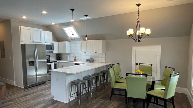 A modern kitchen with a central island, stainless steel appliances, and a dining area with green chairs. - 4th Street Mkt Apt 302: Convenient Walk to Main Street | 2BR Apt in Highlands (Highlands)