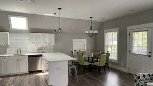 A modern kitchen with white cabinetry, a central island, and a dining area with green chairs. - 4th Street Mkt Apt 302: Convenient Walk to Main Street | 2BR Apt in Highlands (Highlands)