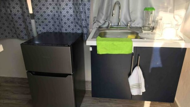 Una cucina compatta con un frigorifero in acciaio inox, un lavello con un asciugamano verde e un pavimento in legno con un tappetino di benvenuto.