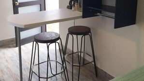 Una cucina compatta con un piano di lavoro bianco, due sgabelli e un piccolo ripiano con un asciugamano arrotolato.