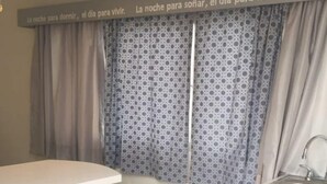 Una cucina compatta con un piano di lavoro bianco, uno sgabello da bar e una finestra con tende a motivi.