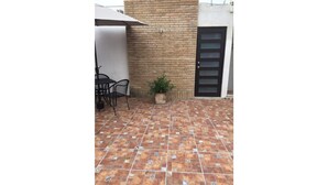 Un patio con pavimento piastrellato, un muro in mattoni, una porta nera e una piccola pianta in vaso.
