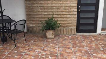 Un patio con suelo de baldosas, pared de ladrillo, puerta negra y una pequeña planta en maceta.