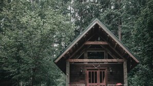 Una cabaña de madera con balcón, rodeada de un bosque denso.