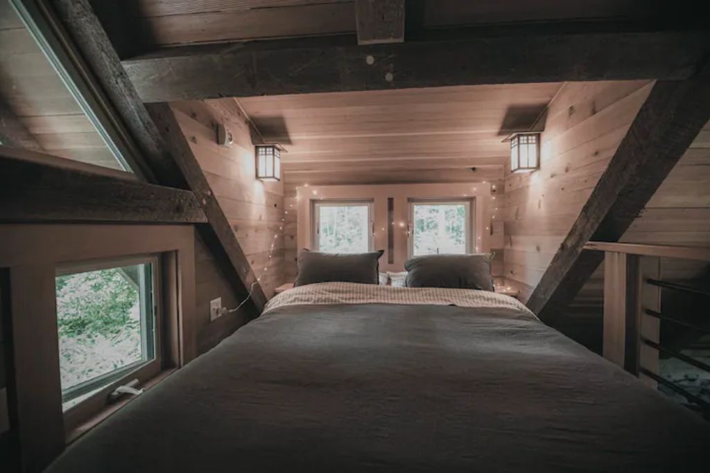 A cozy attic bedroom with a large bed, two windows, and two wall-mounted lanterns.