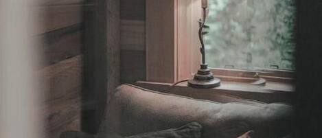 Une pièce chaleureuse avec un décor intérieur en bois, une fenêtre donnant sur les arbres et une lampe posée sur le rebord de la fenêtre.