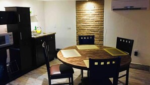 A compact kitchen with a round wooden table, two chairs, a microwave, and a brick accent wall. - My Depa Cinnamon In the Center of Cd. valleys (Ciudad Valles)