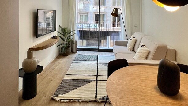 A modern living room with a round wooden dining table, a sofa, and a large window with a view of buildings. - 11 Reyes Catolicos Premium Homes - Deluxe Homes (Alicante (Alacant))