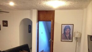A living room with a black sofa, a red rug, a wooden door, and a framed picture on the wall. - My Depa Waterfall In the Center of Cd. valleys (Ciudad Valles)
