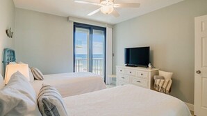 A hotel room with two beds, a TV, a ceiling fan, and a balcony with a view.