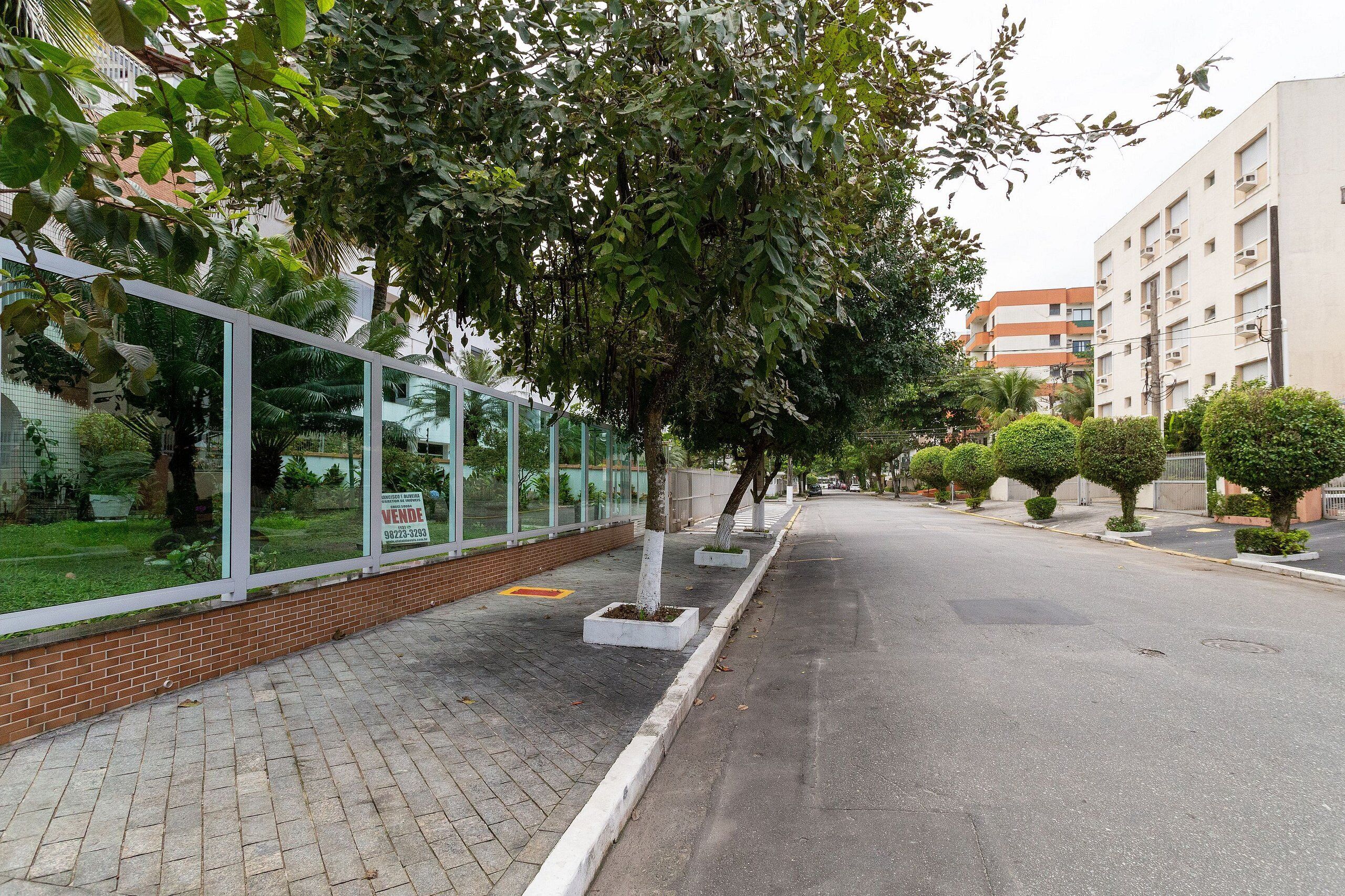 Una calle con acera, árboles y un edificio con un cartel de 'For Sale'.