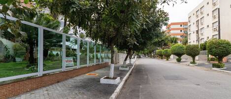 Una calle con acera, árboles y un edificio con un cartel de 'For Sale'.