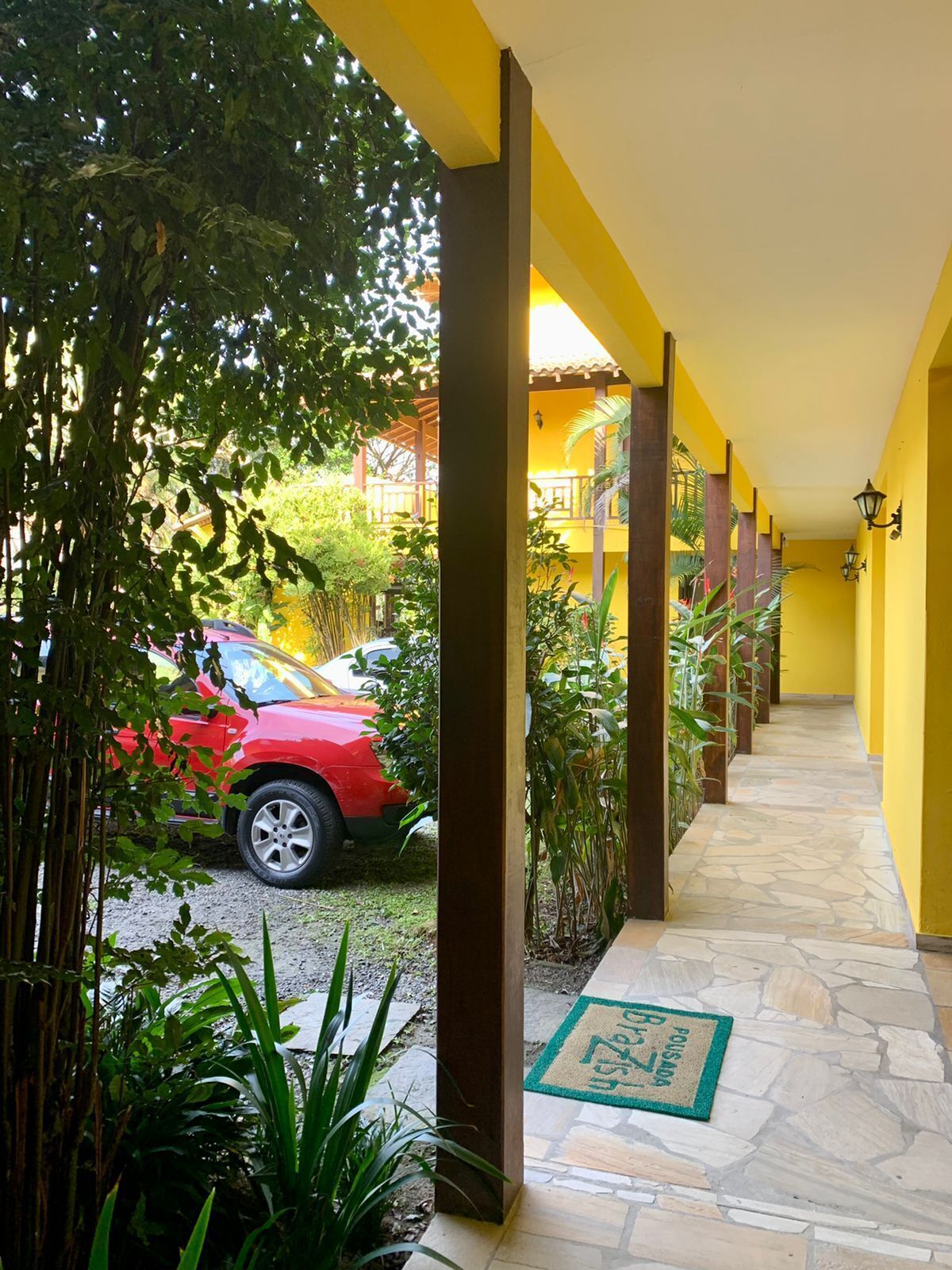 A covered walkway with yellow walls, stone flooring, and a red car parked outside.