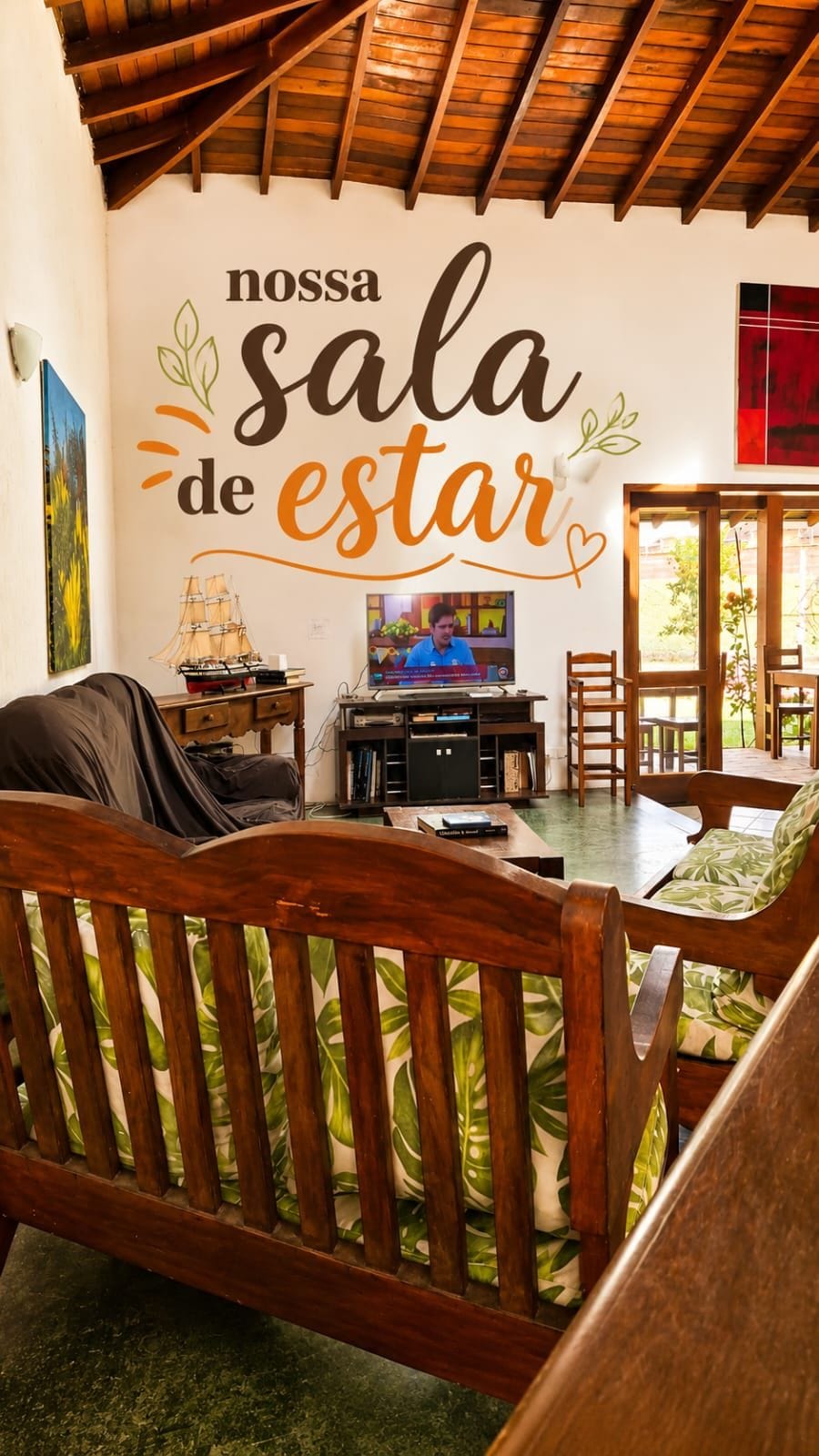 A cozy room with a wooden ceiling, a television, a bookshelf, and a wall with a motivational quote.