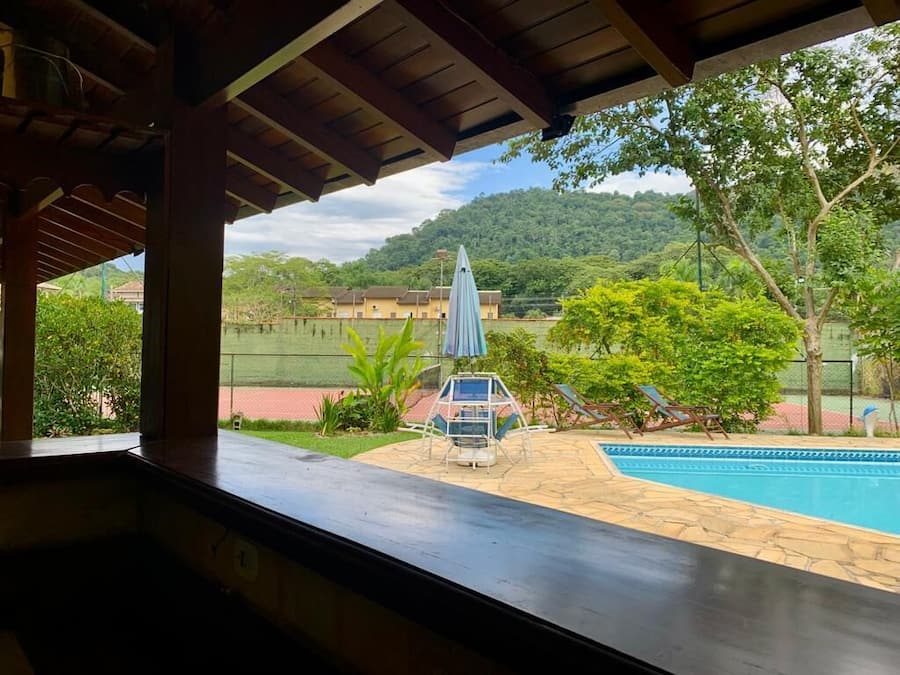 Vista desde un espacio cubierto con vista a una piscina, con un mirador y sillones de descanso al frente y un paisaje montañoso en el fondo.