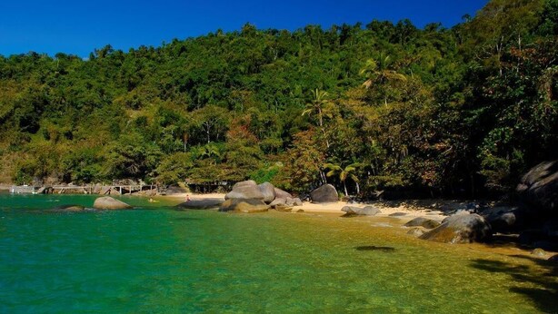 Une plage tropicale avec une eau turquoise et limpide, de gros rochers et une végétation luxuriante en arrière-plan.