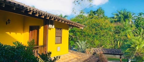 Un edificio giallo con tetto in tegole, circondato da vegetazione lussureggiante e un cielo azzurro intenso.